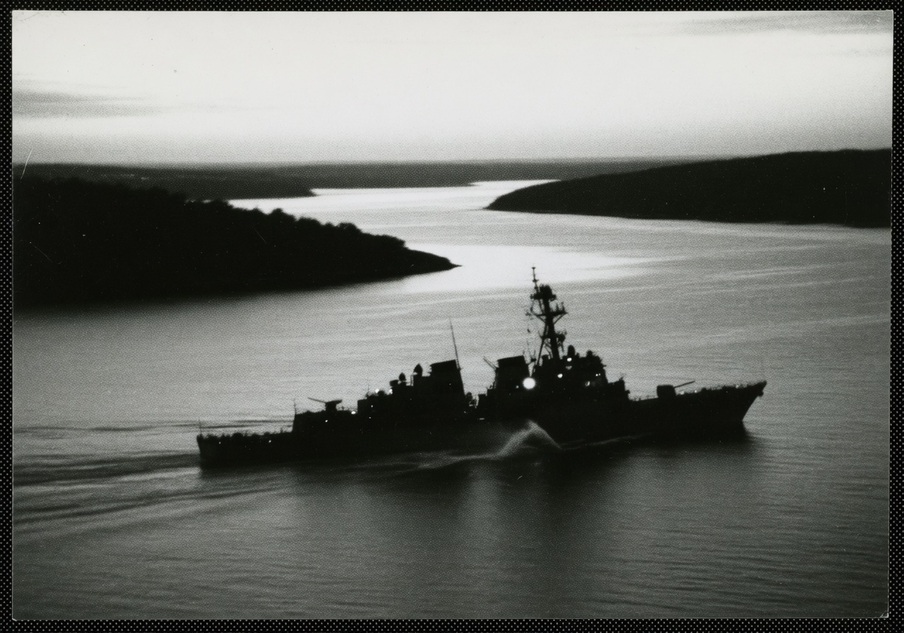 High-contrast monochrome wire-photo composition: the silhouette of a guided-missile destroyer cutting low across a narrow strait, plume of spray off the bow, faint signal grain across the frame, a single ship lamp catching as a hard pale point. No flags, no insignia, no text.