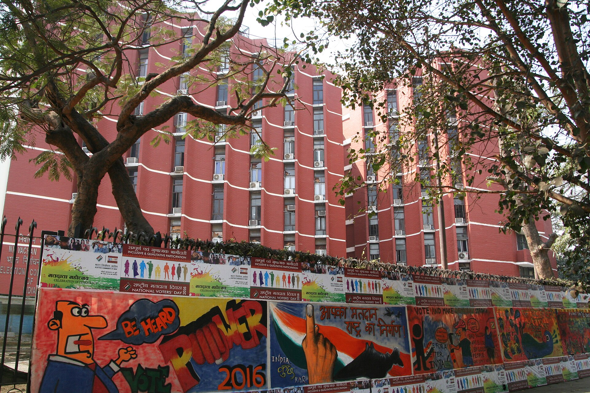 Election Commission Headquarters building in New Delhi, with National Voter Day posters outside.