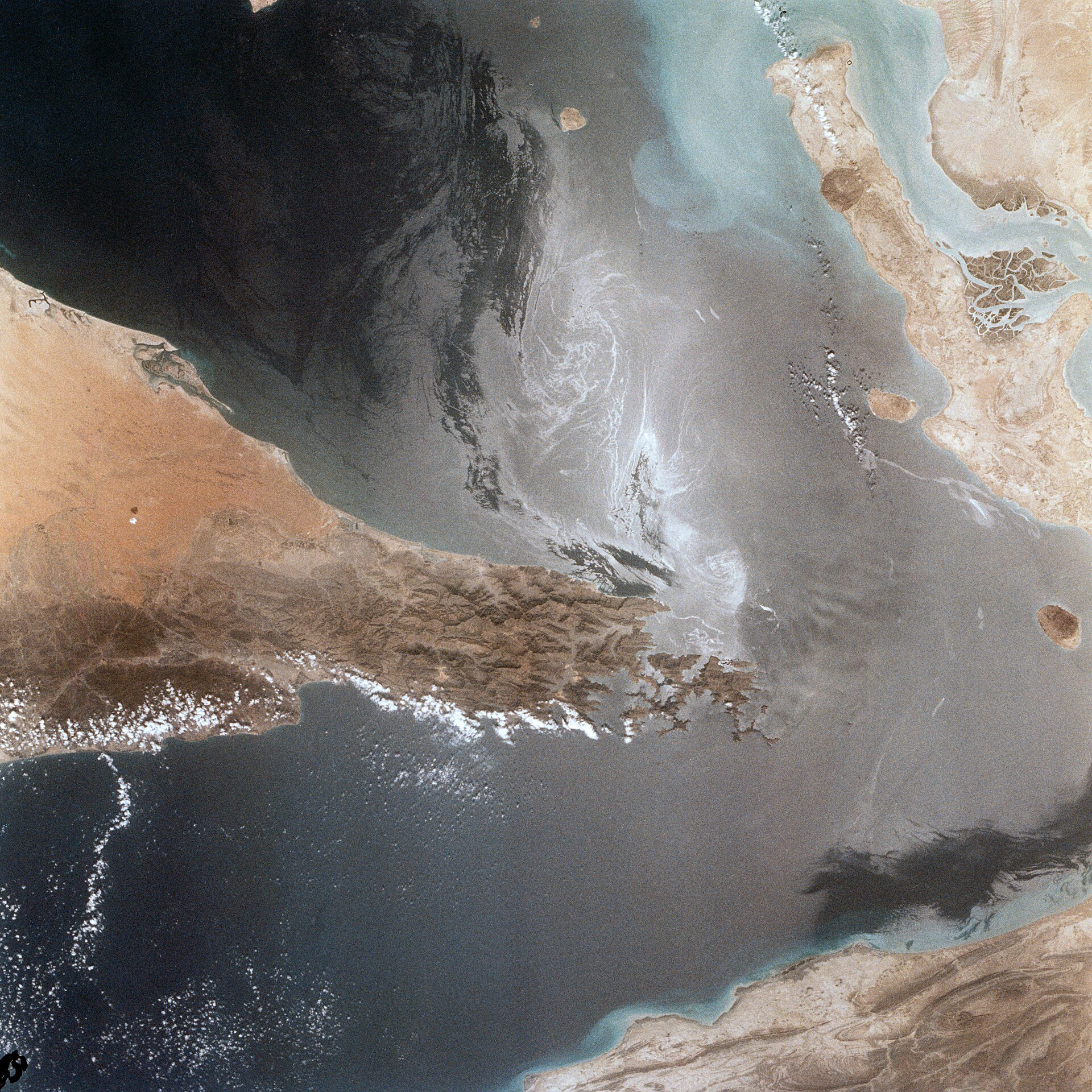 View from space of the Strait of Hormuz, showing portions of Oman, the United Arab Emirates and Iran, with ship wakes visible in the strait and Qeshm Island off the coast of Iran.