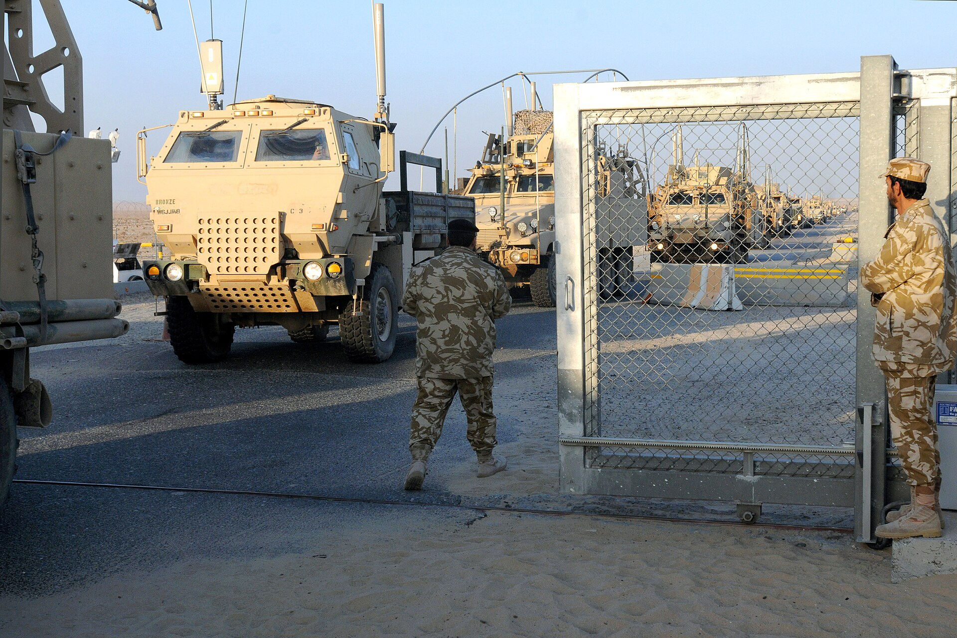 Kuwaiti soldiers look on as the last U.S. convoy crosses the border into Kuwait from Iraq.